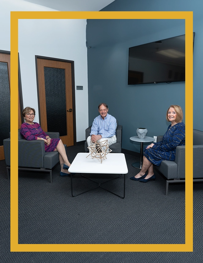 Three people sitting in a room with tables and chairs.