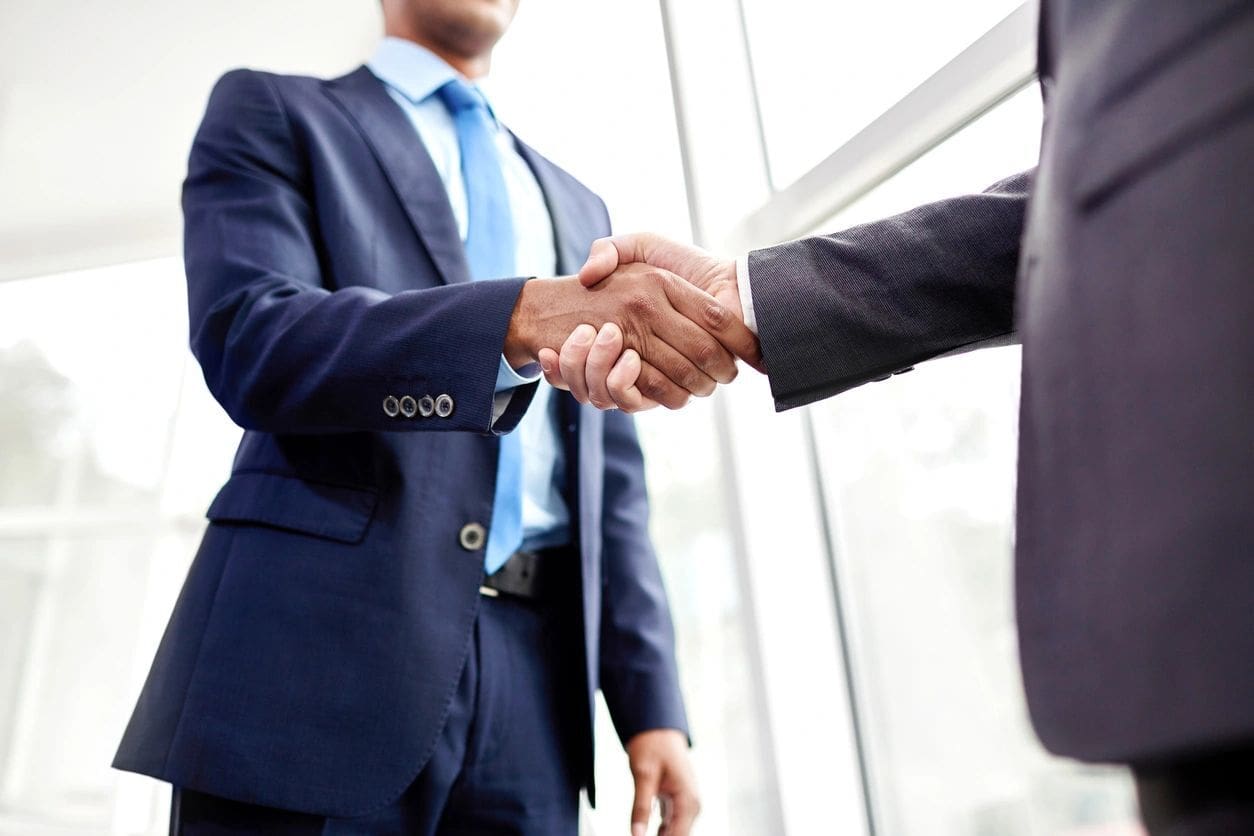 Two men in suits shaking hands over a window.